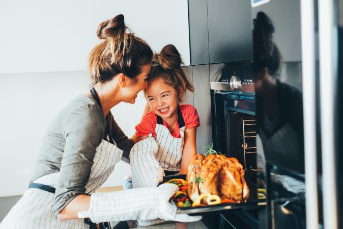A woman and a girl in aprons take a roasted turkey out of an oven. Open larger view.