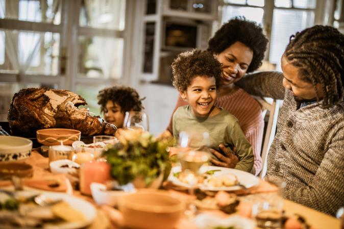 Smiling children and adults at a table set with a roast and side dishes. Open larger view.