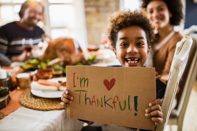 A boy holds a sign that reads “I’m Thankful!” at a family table. Open larger view.